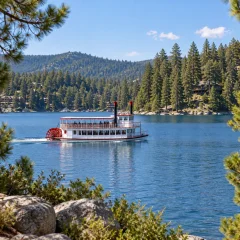 A classic paddlewheel tour boat crossing a pine-lined mountain lake